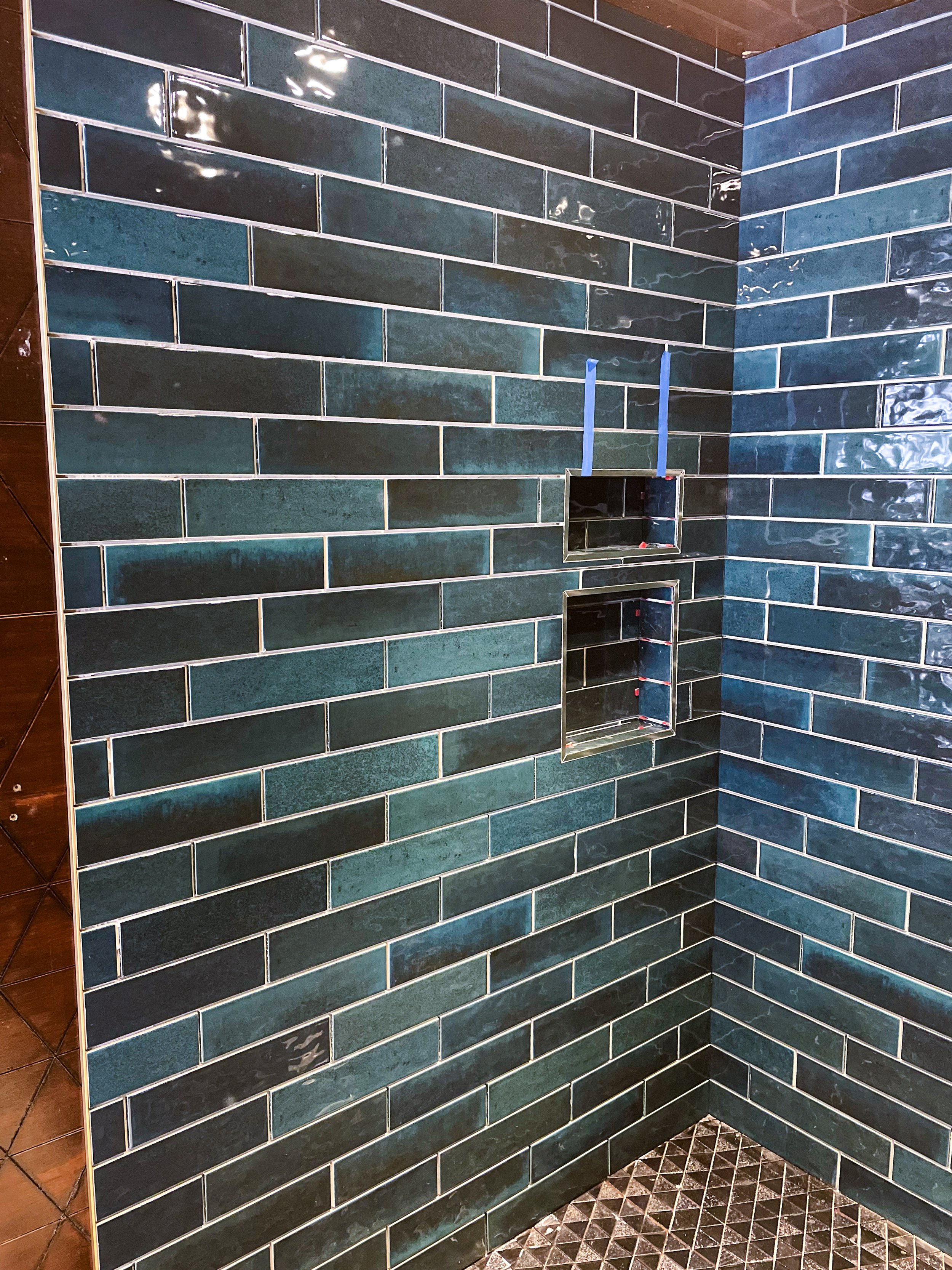 Green and blue ceramic tile shower with two built-in wall niches and two blue shower poles.
