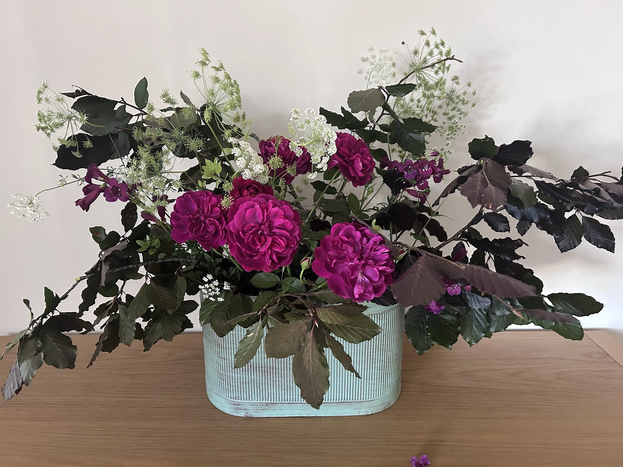 Arrangement of pink and purple flowers and greenery in a textured green container on a wooden surface.