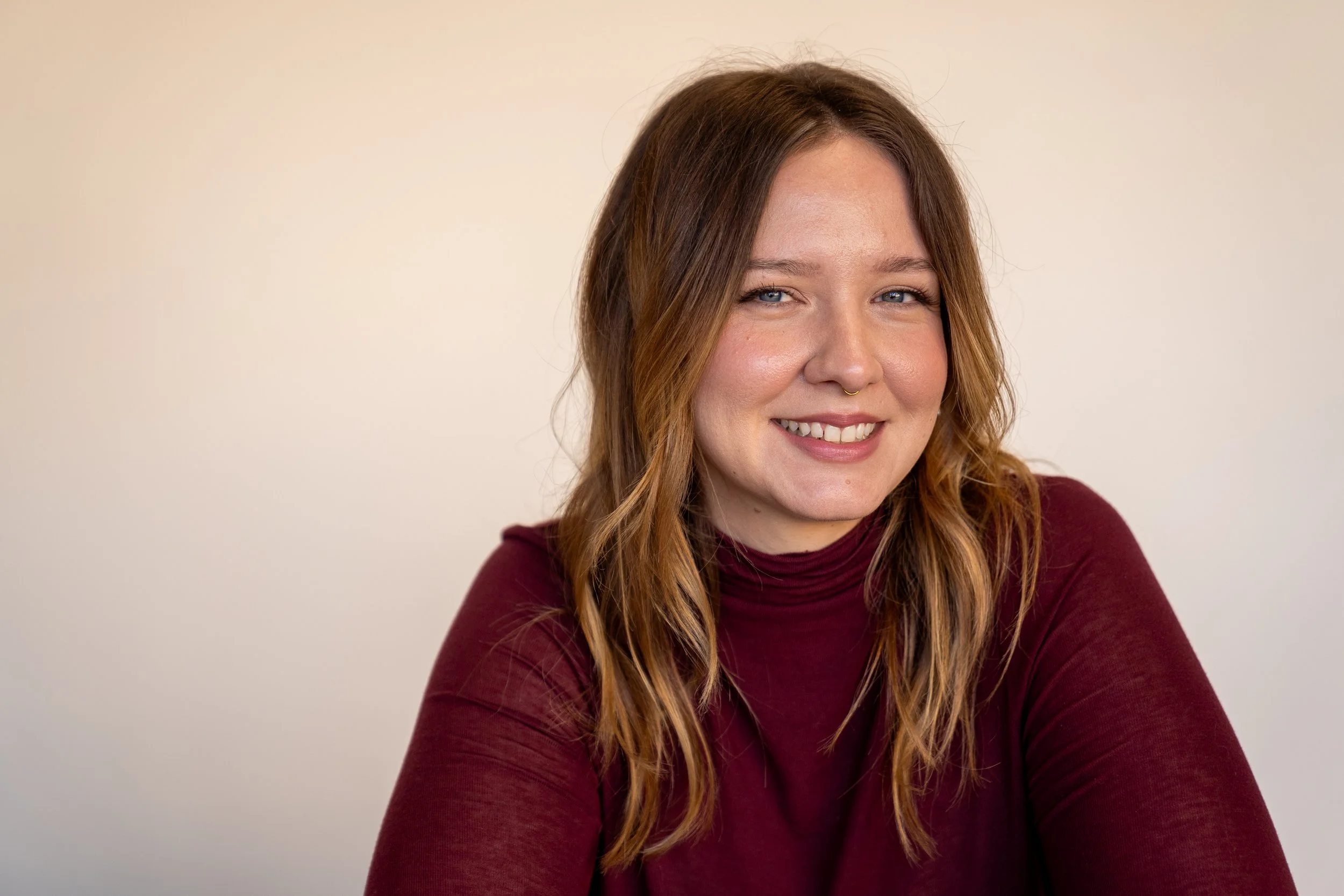 A woman with shoulder-length wavy hair, wearing a maroon turtleneck, smiling and looking at the camera against a plain background.