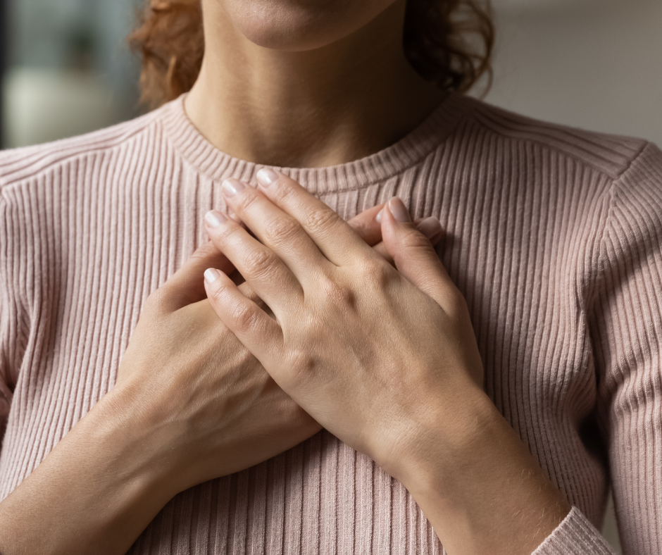 Close-up of a woman with her hands placed over her heart in a self-soothing gesture, illustrating self-compassion in ACT-I.