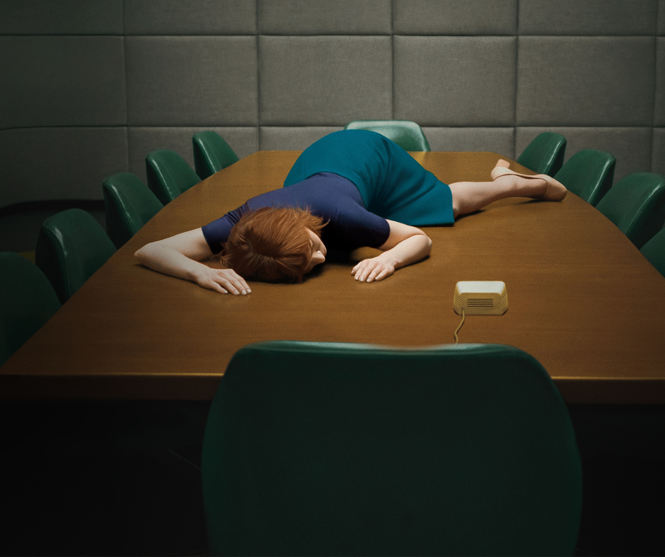 Helly R. from Severance lying face down on a large conference table, illustrating the transition from the active energy of fawning to the total system shutdown and exhaustion of the flop or collapse response.