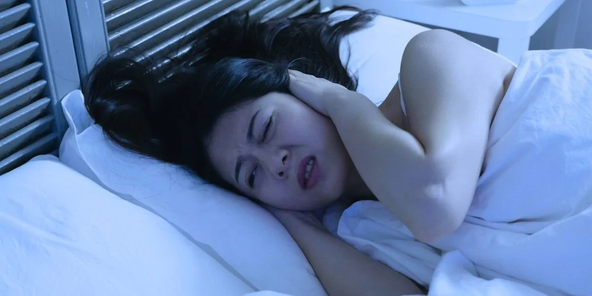 Frustrated woman lying awake in bed at 12:34 AM, representing emotional reactivity and sleep anxiety.