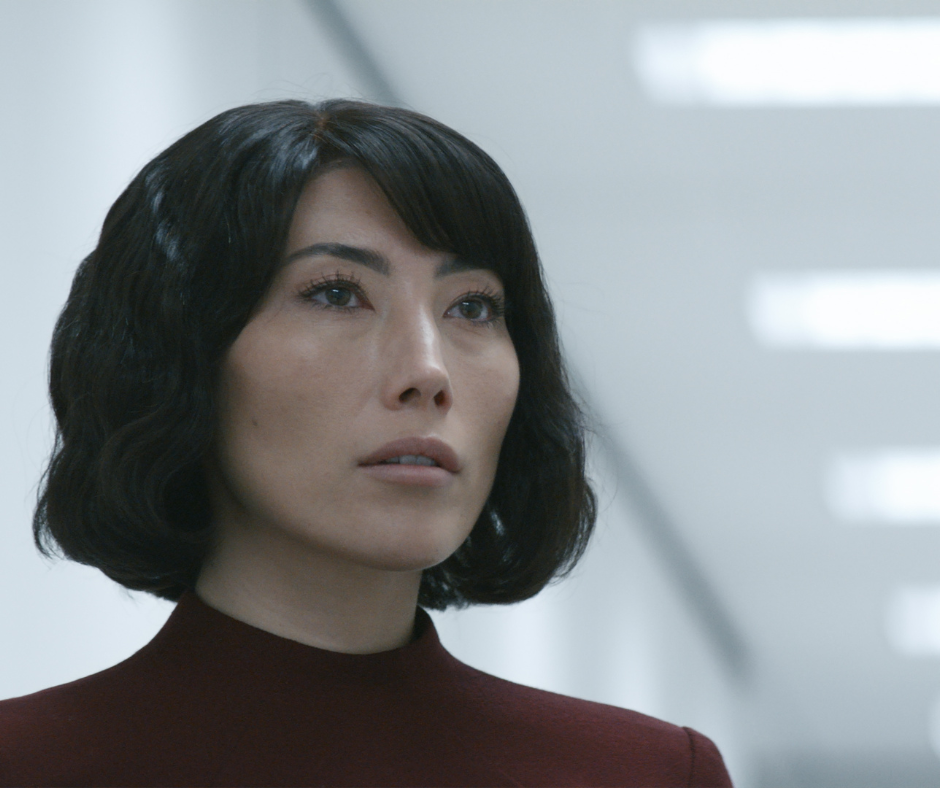 A still of Miss Casey from the TV show Severance, illustrating the fawn trauma response and the 'submit' survival reflex through her calm, compliant, and self-sacrificing demeanor.