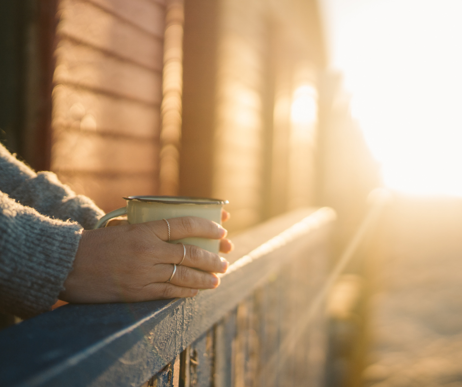 Close-up of hands holding a mug on a balcony at sunrise, representing living a meaningful life regardless of sleep quality.