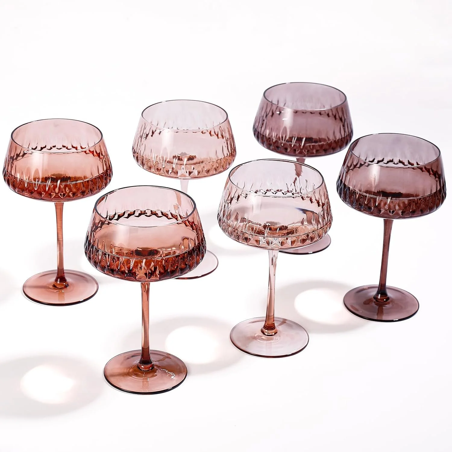 Six pink tinted wine glasses with textured patterns, placed on a white surface with shadows.