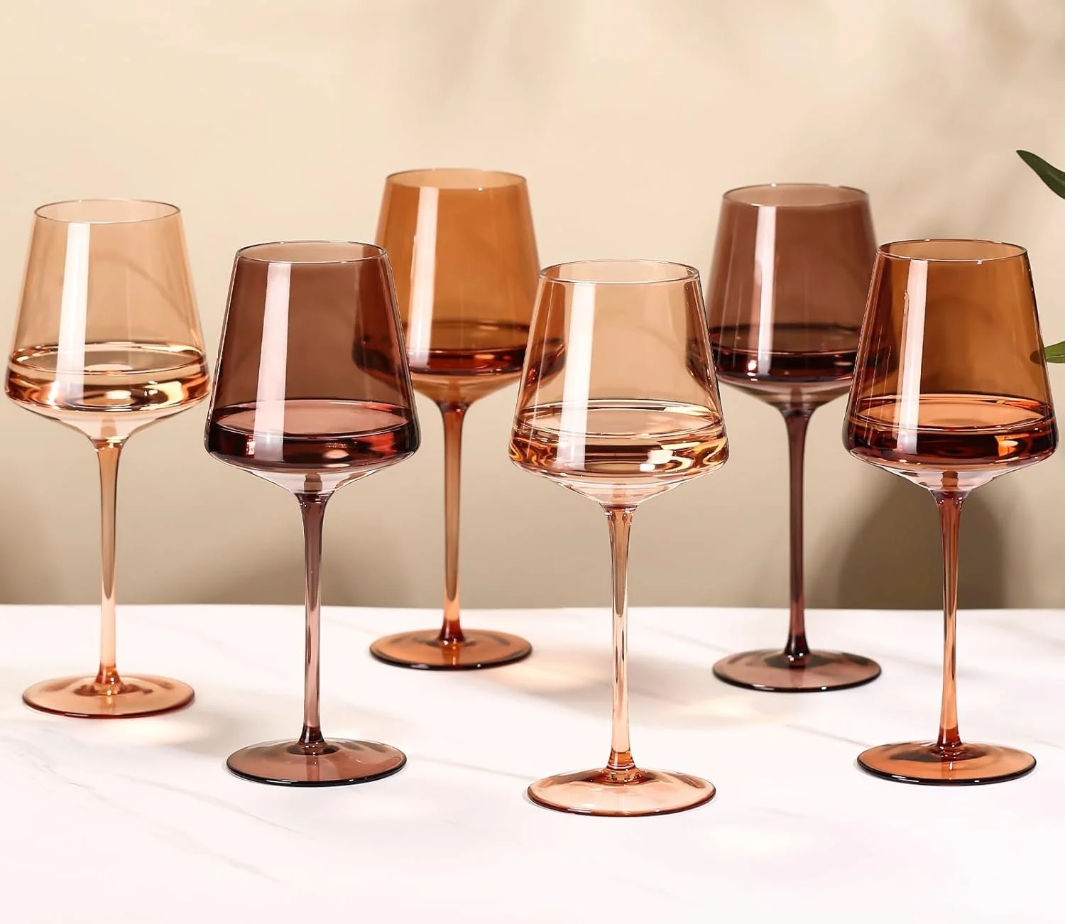Six wine glasses with pink and brown tinted glassware, some filled with rosé wine, placed on a white surface with a light-colored background.