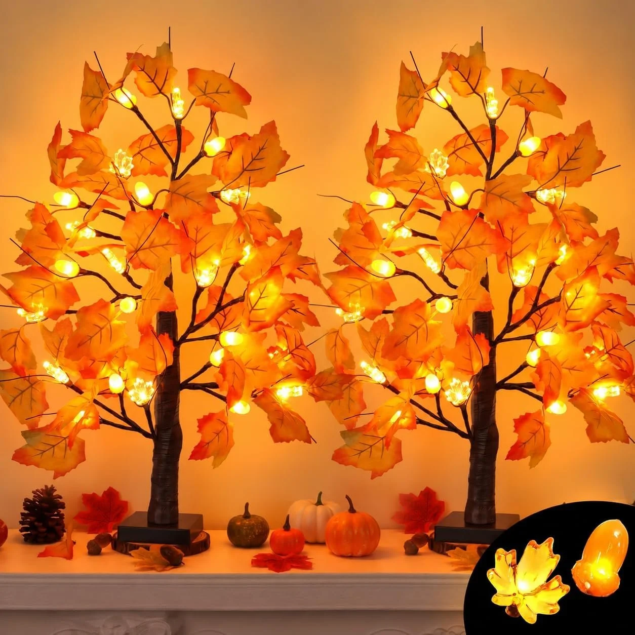 Decorative autumn-themed table display featuring two illuminated artificial maple trees with orange leaves, surrounded by pumpkins, gourds, pine cone, and autumn leaves.