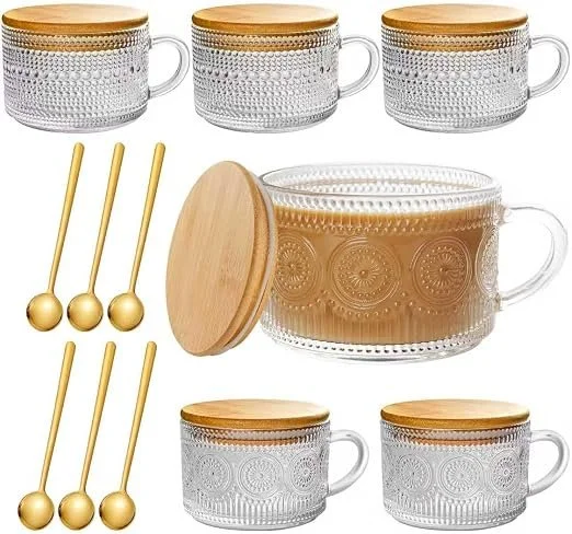 Six clear glass cups with gold-colored lids and a matching glass jar with a wooden lid, all featuring decorative patterns. Accompanying these are six gold-colored stir sticks.