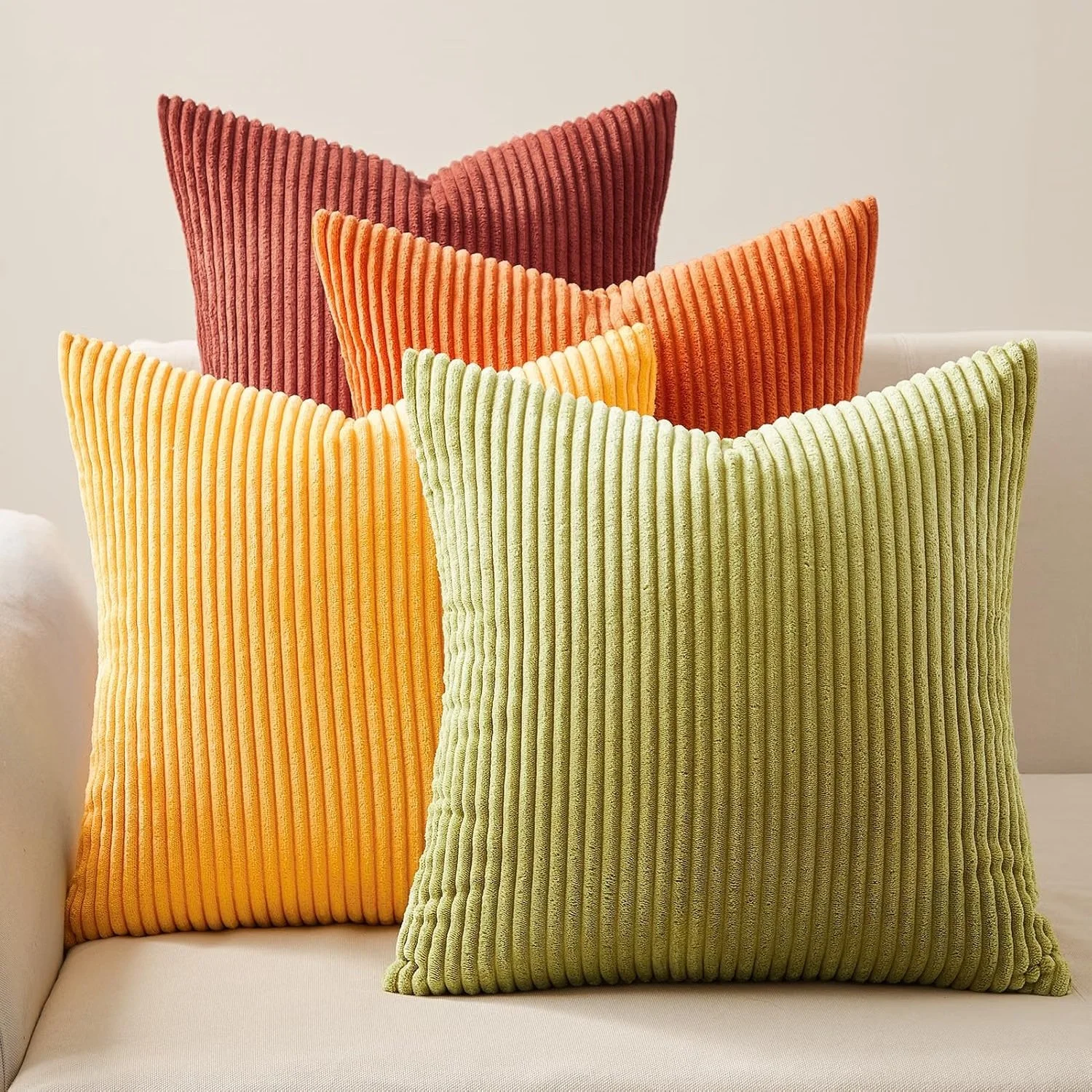 Four colorful corduroy throw pillows on a white sofa, in shades of green, orange, yellow, and rust.