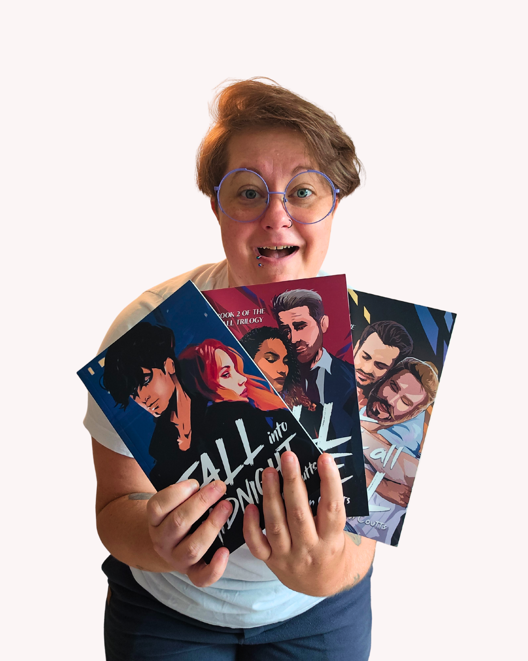 Person with short hair, wearing glasses, smiling, holding three graphic novels about LGBTQ+ themes.