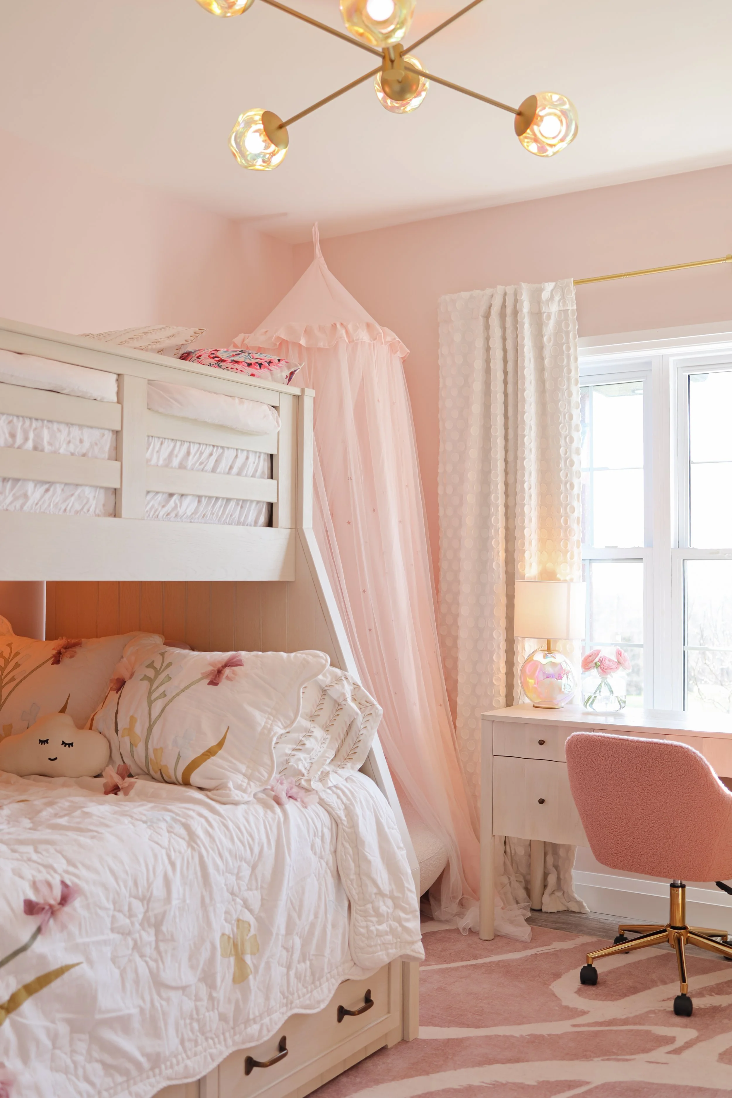 A pink-themed bedroom with a bunk bed, pink canopy, white nightstand, pink office chair, and window with pink and white curtains.