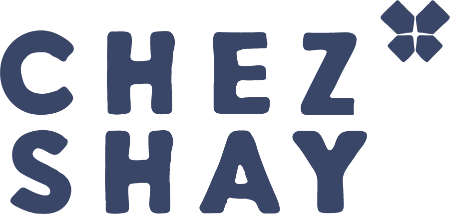 The image shows the text 'CHEZ SHAY' with a stylized flower or geometric shape in the top right corner, all in dark blue on a black background.