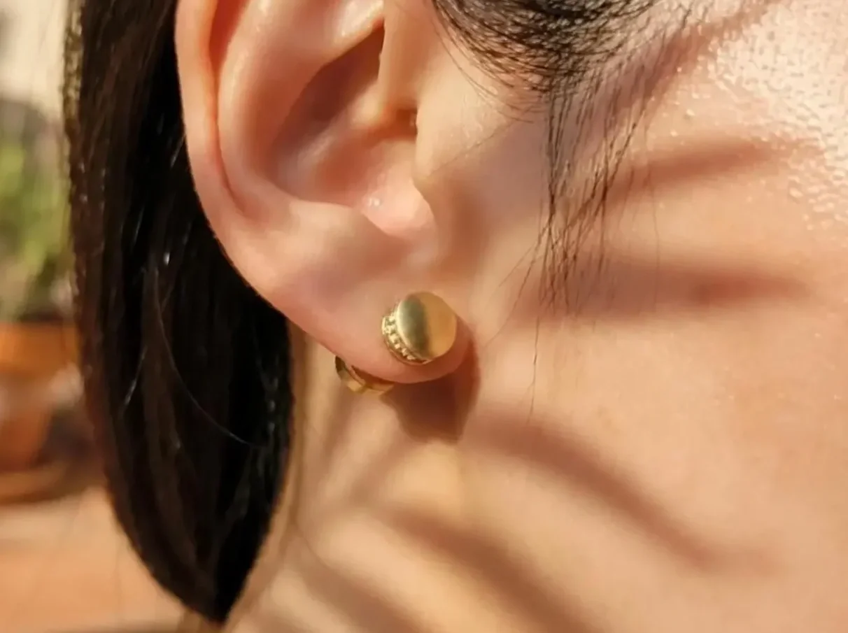 Close-up of a person's ear wearing a gold tone diffuser stud earring and with a summer mood in the foreground.