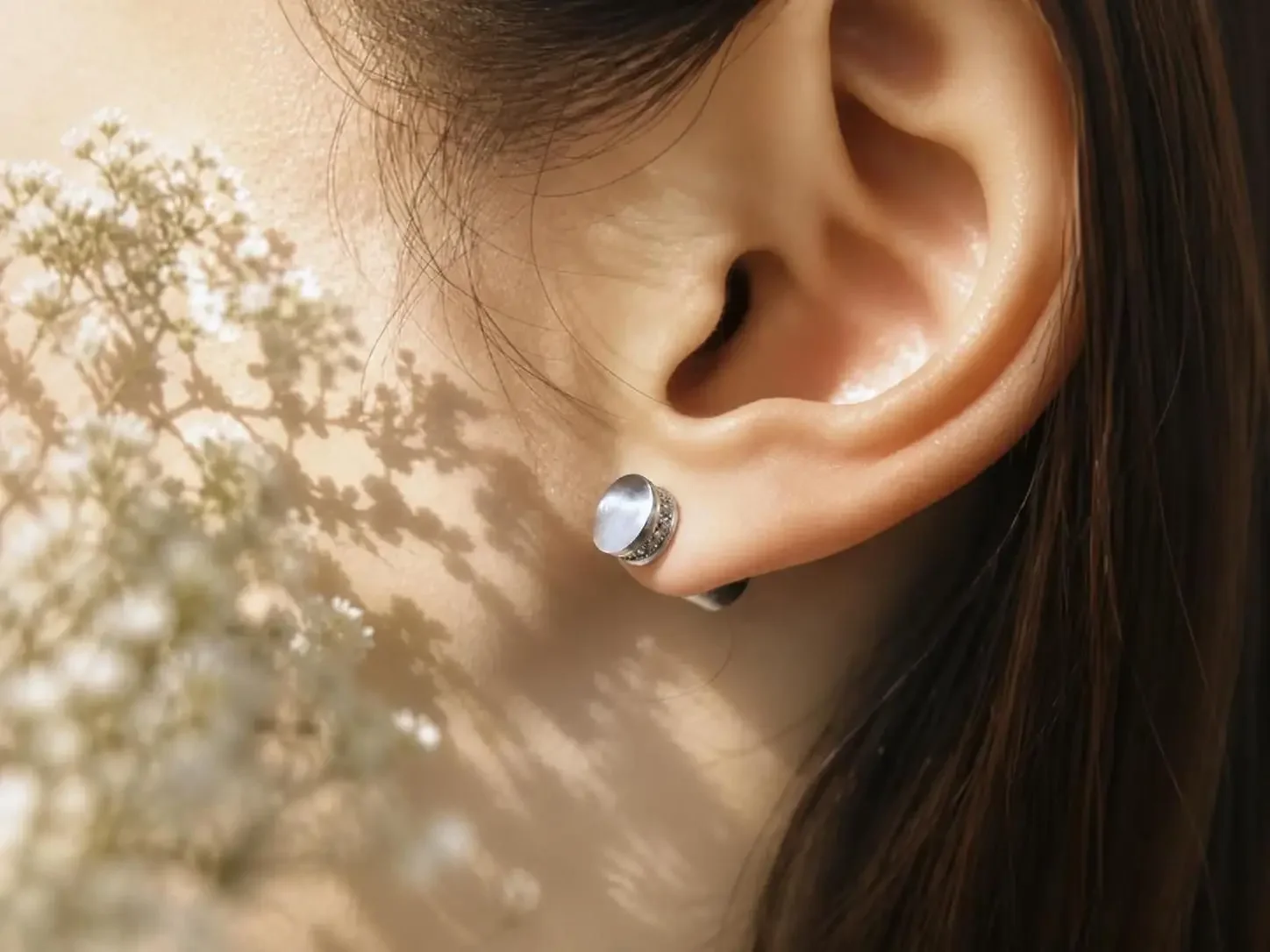 Close-up of a woman's ear with a silver tone diffuser stud earring and with a spring mood in the foreground.
