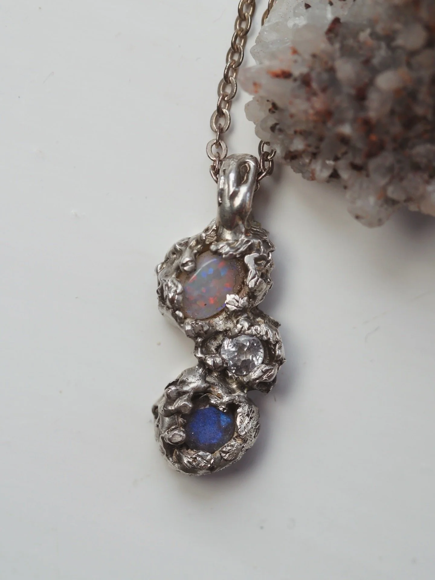 Close-up of a silver charm bracelet with various textured circular charms, set against a white background with some rocks visible.