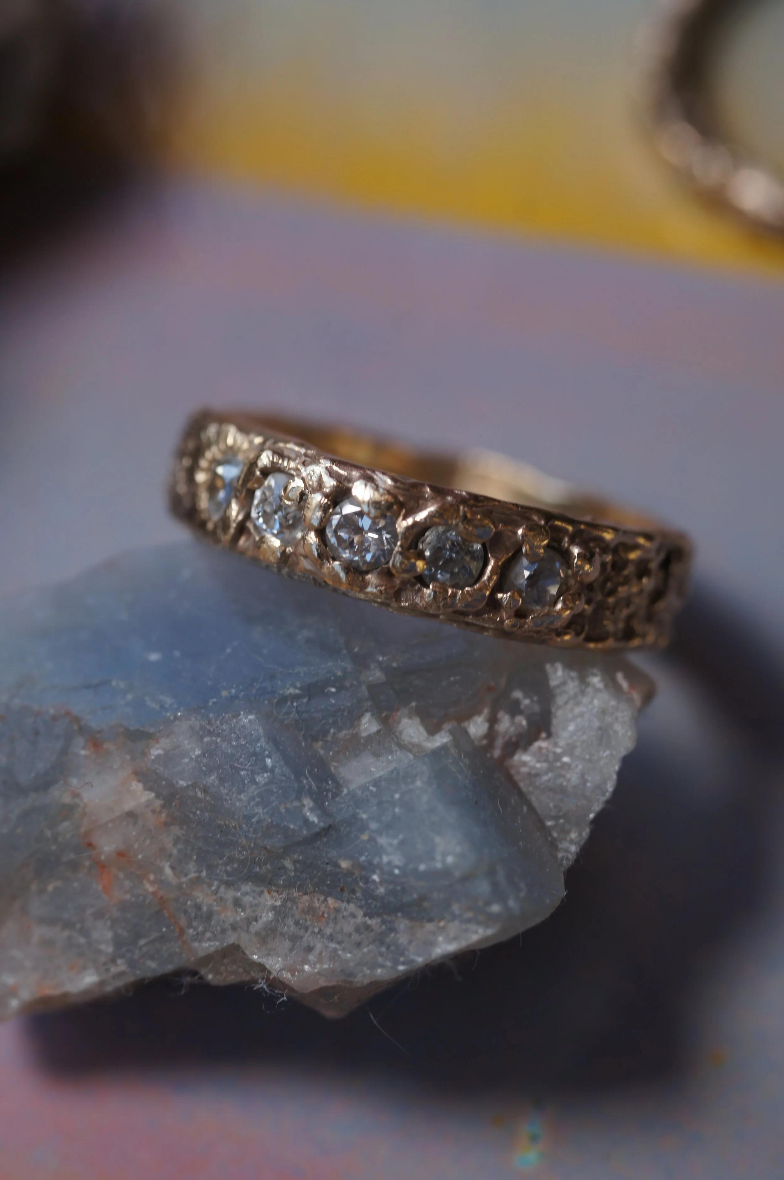 Close-up of a ring with diamonds resting on a rough rock surface.