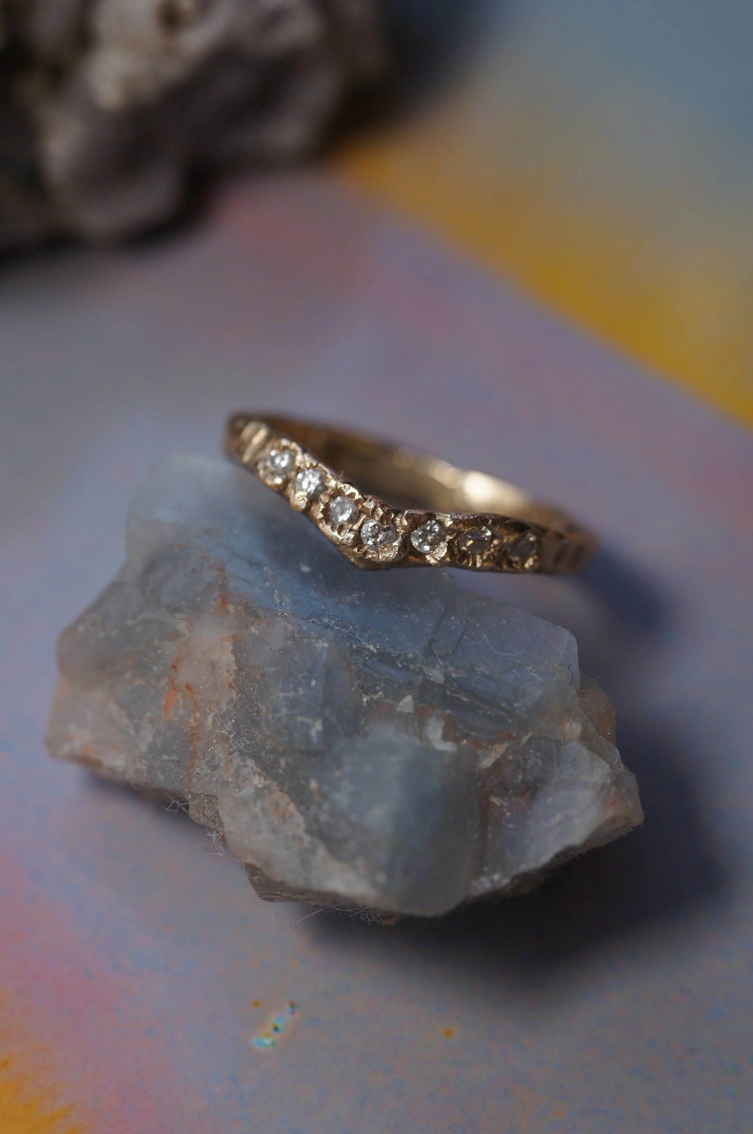 Close-up of a gold ring with small diamonds, placed on a clear quartz stone with a multicolored background.