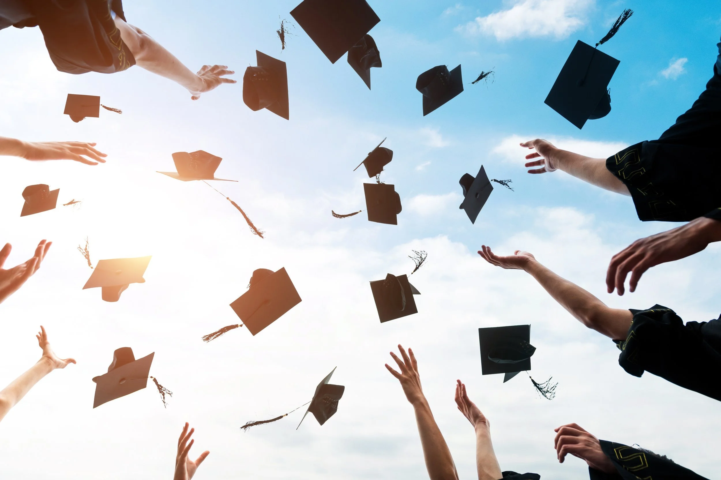 Graduates in caps and gowns throwing their caps into the sky during a graduation ceremony.