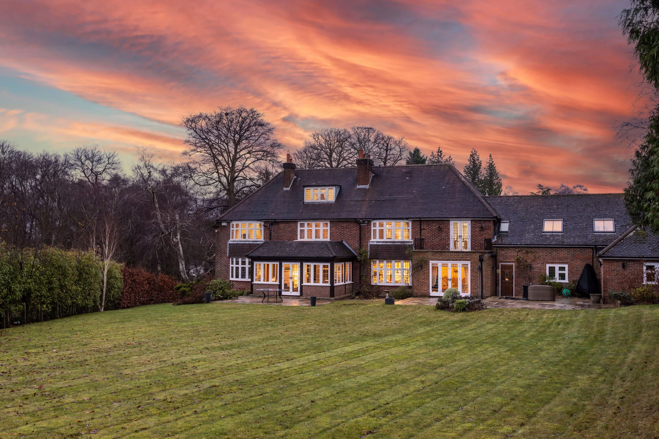 Large brick house with multiple windows and a spacious backyard under a colorful sunset sky.