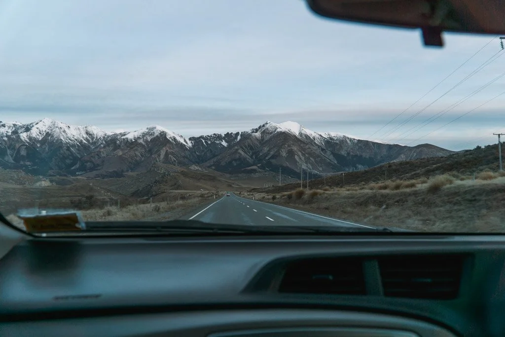 Snowy mountains and an open road through the windscreen of a car