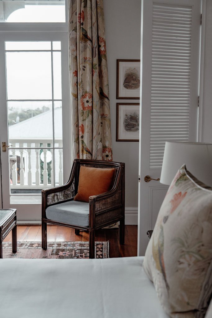 A hotel room with wooden floors, persian rug and french doors opening onto a balcony