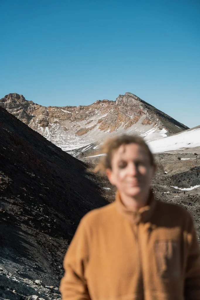 An out of focus woman stands in front of a view of a volcanic background