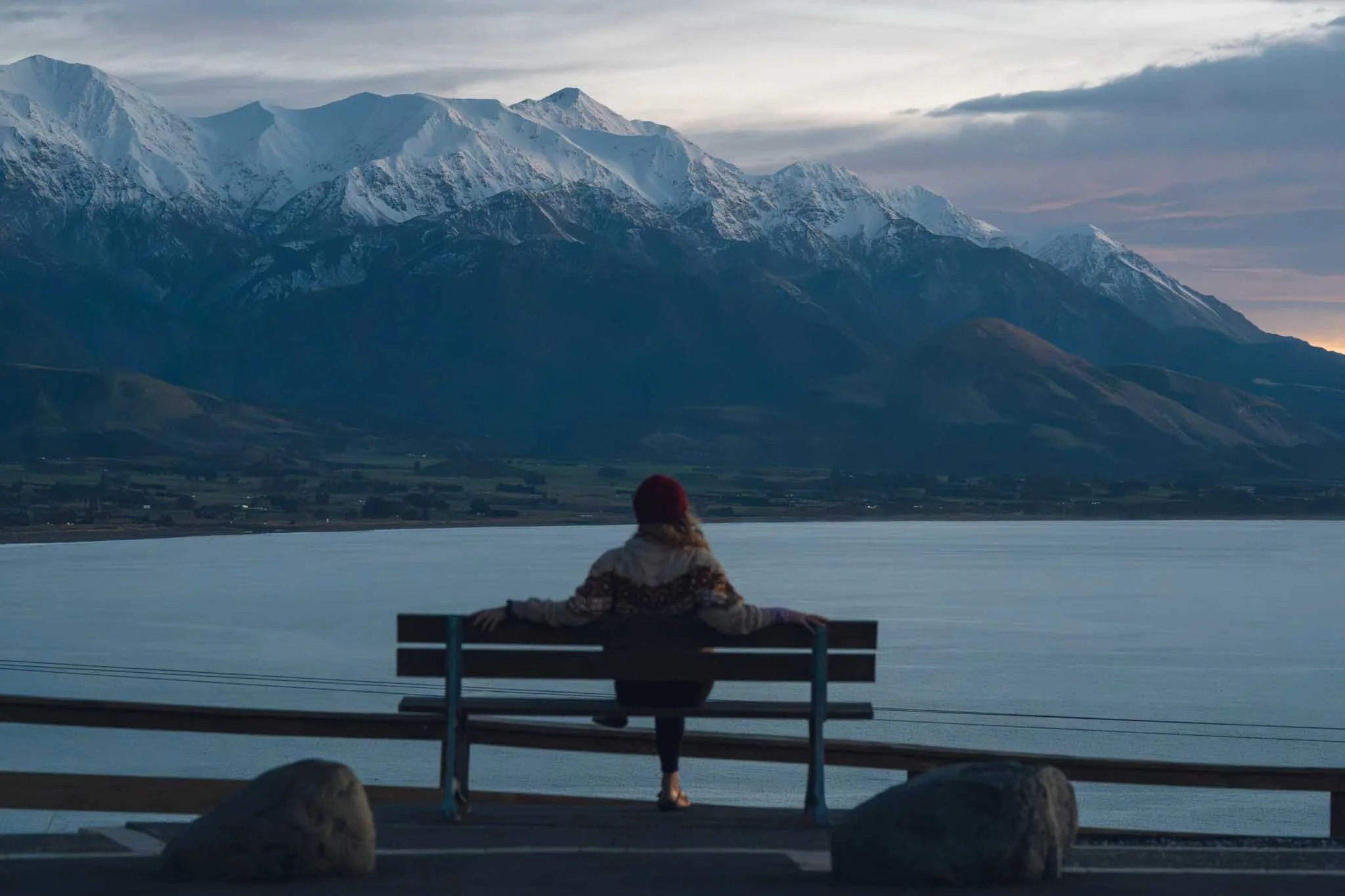 A person sits on a bench overlooking the Kaikoura mountains and coastline