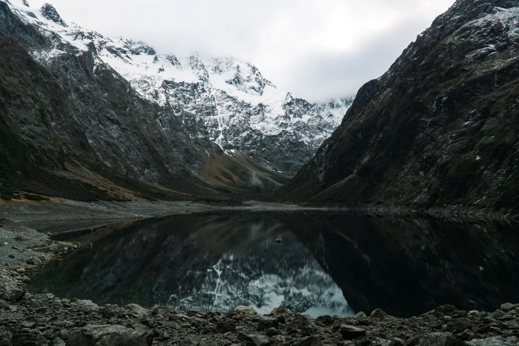 The black water of Lake Marian reflects snowy mountains