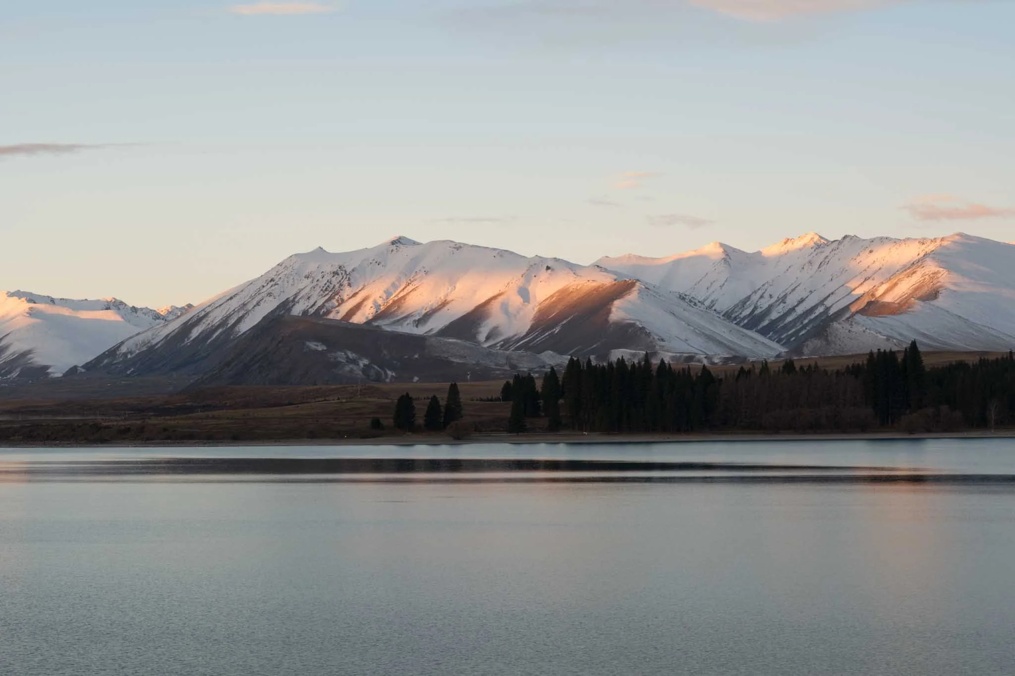 Sunset illuminates the snowy mountains on the edge of lake tekapo