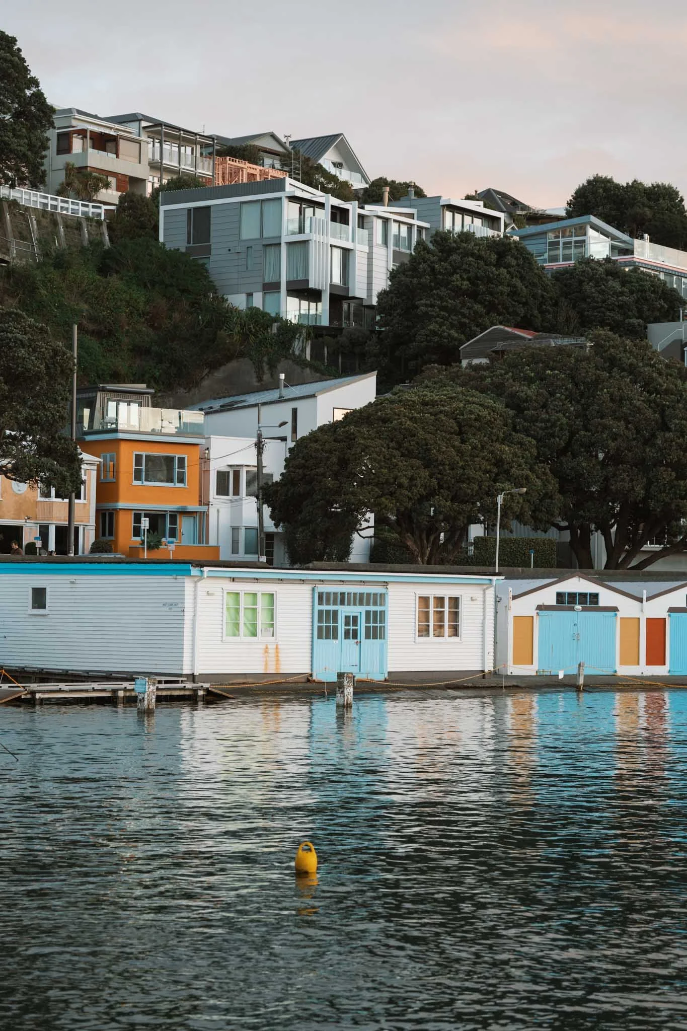 Boatsheds with red, orange, and blue doors line Wellington's waterfront
