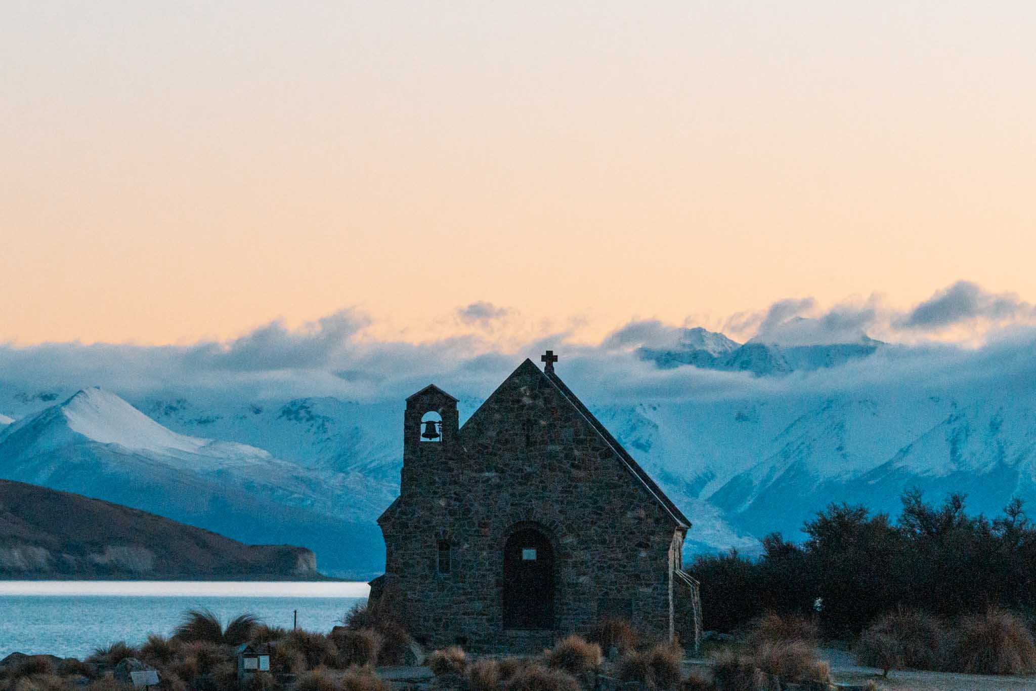 Snow capped hills are bathed in dawn light behind the Church of the Good Shepherd