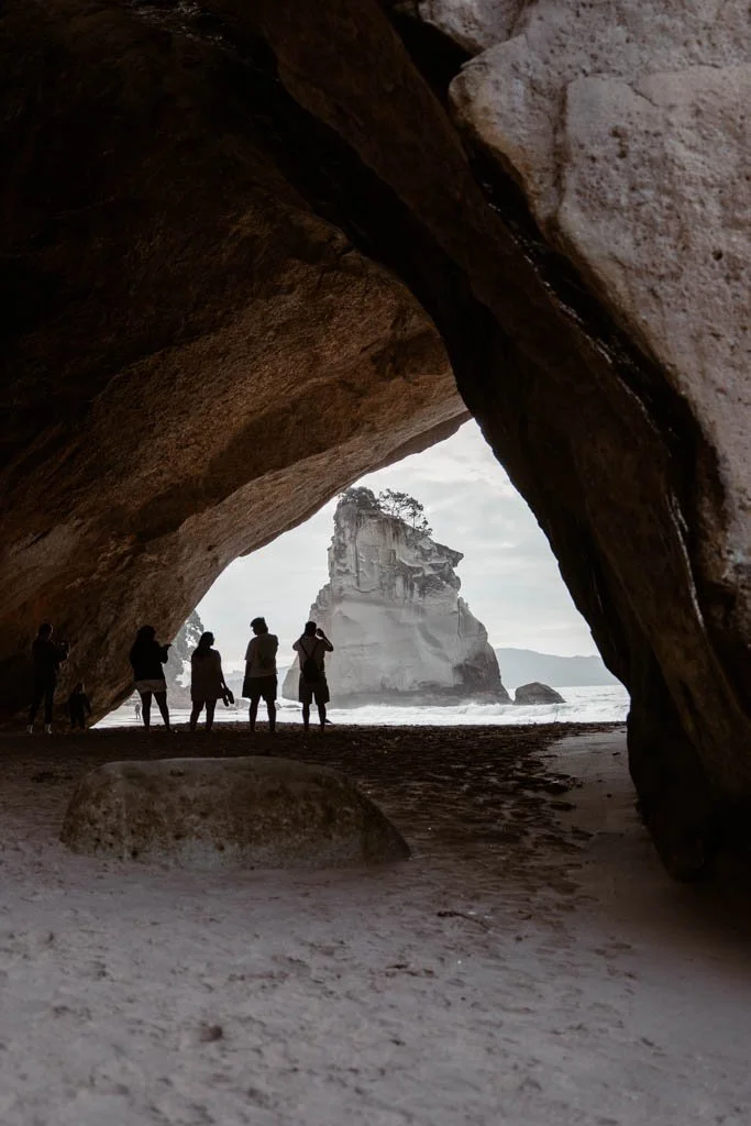Four people stand silhouetted in the arch at Cathedral Cove