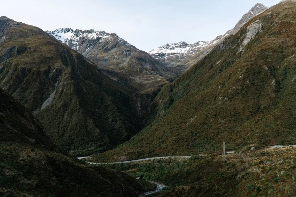 A narrow road weaves through snowy mountains in Arthur's Pass, New Zealand