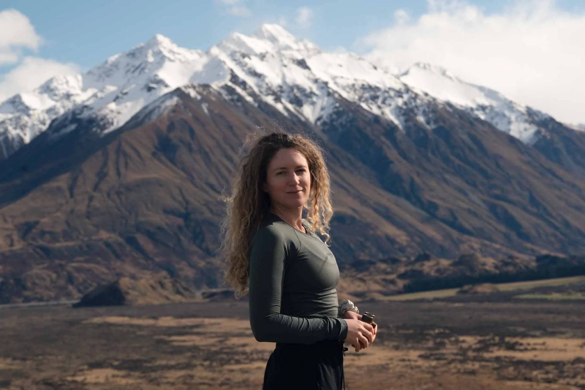 A woman stands in front of a backdrop of snow covered mountains near Mount Sunday in New Zealand