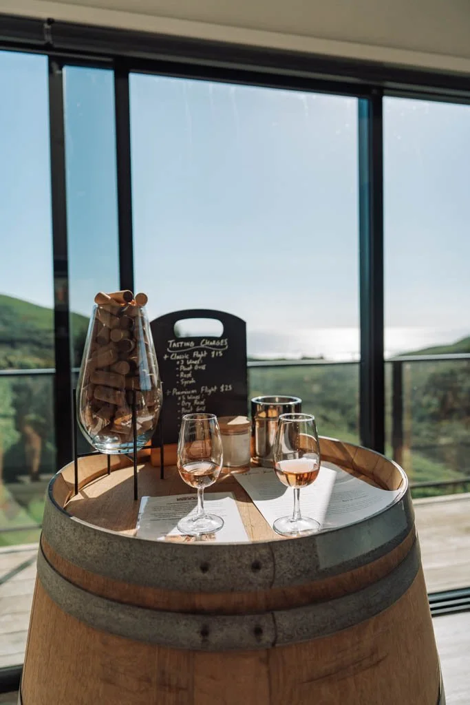Wine tasting at Barrelled Wines, with wine glasses on top of a barrel and the sea visible in the distance