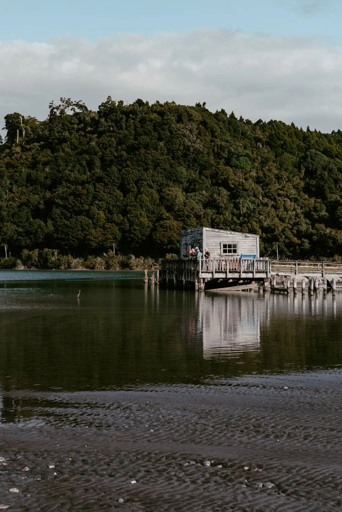 A boatshed is reflected in the still water of Okarito Lagoon