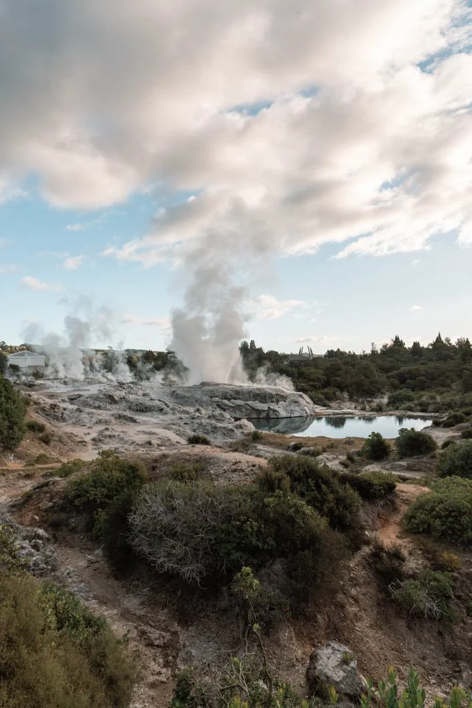 Geysers shoot steam next to a refelctive pool