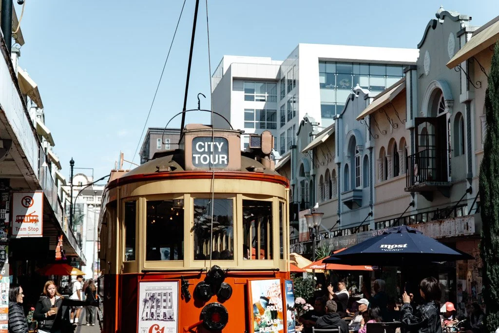 A red and yellow tram trundles between the pastel coloured buildings along New Regent Street in Christchurch