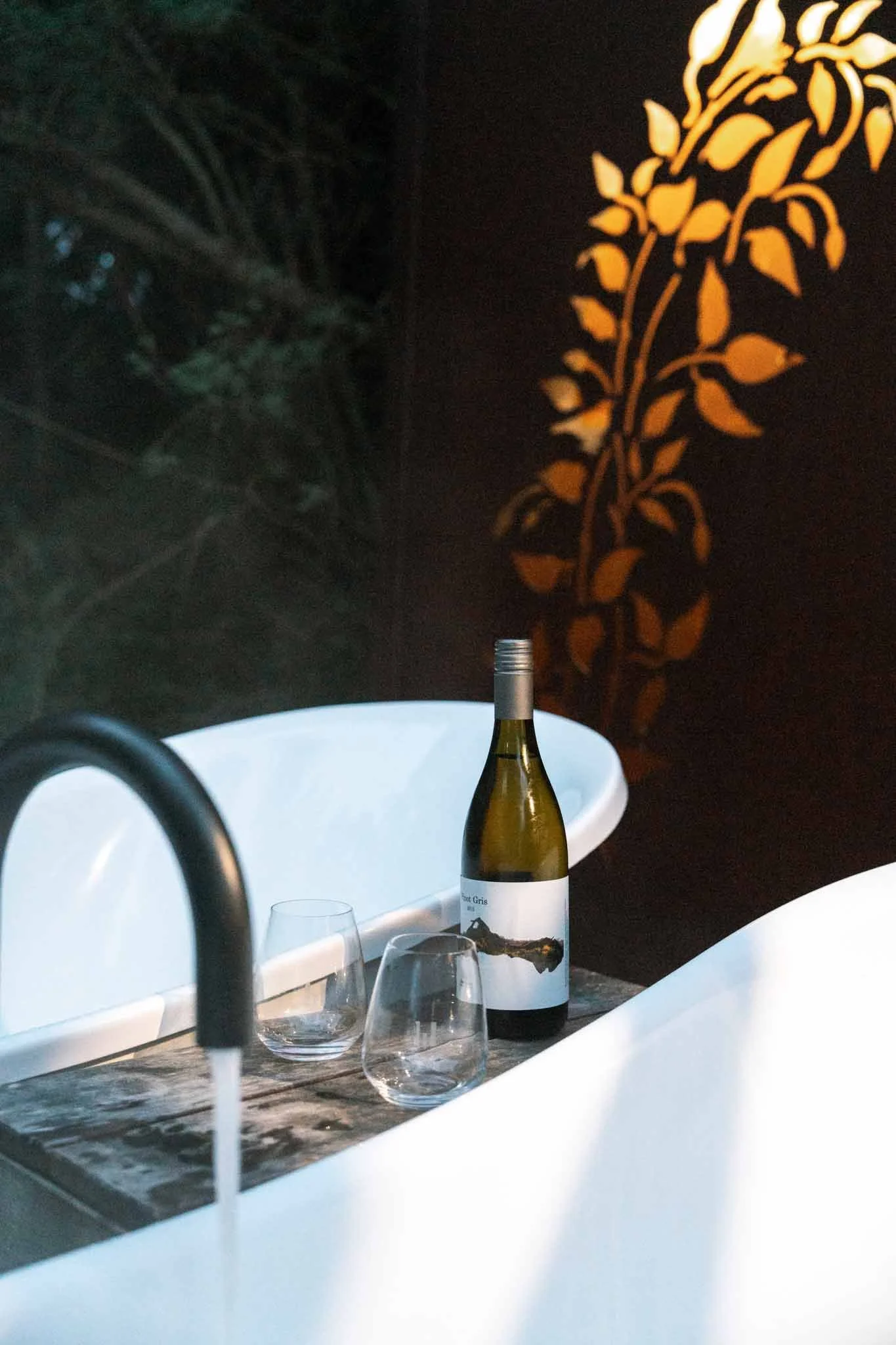 A bottle of wine and two glasses in between two bathtubs