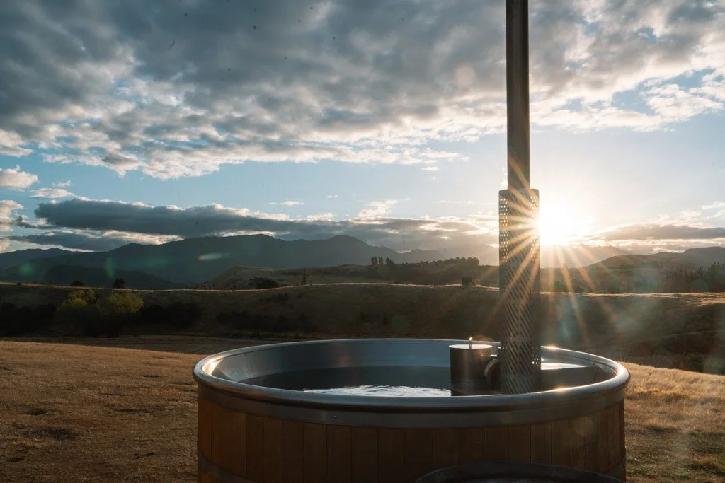 The sun drops down to low hills in the background  - in the foreground is a hot tub