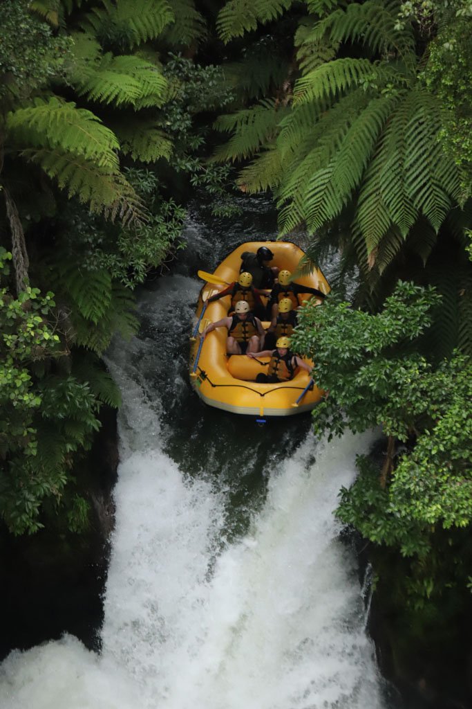 A yellow rafting boat is at the top of a raging waterfall about to tip over the edge