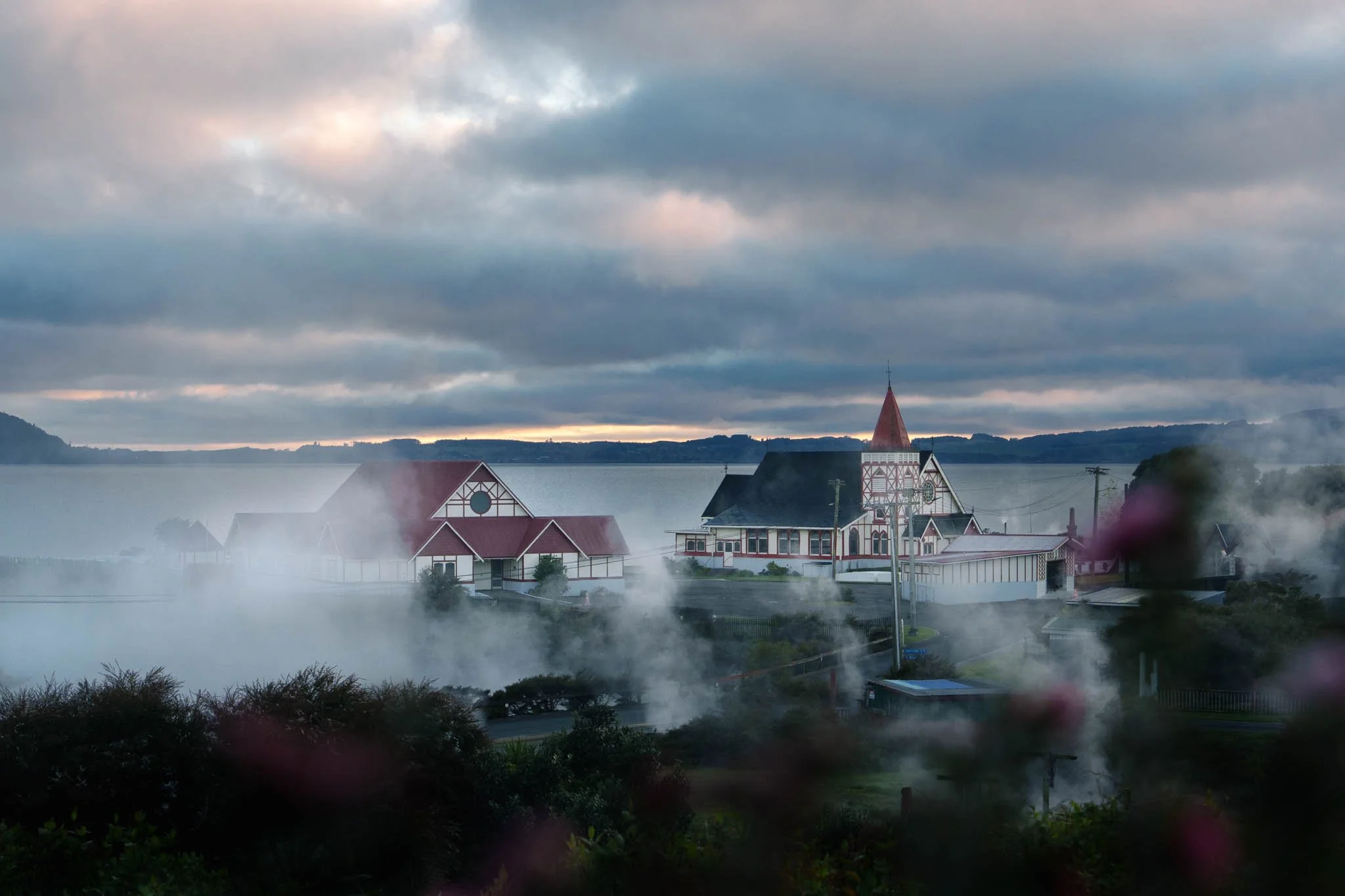 Red and white buildings are clouded with steam from geothermal activity in Ohinemutu, Rotorua