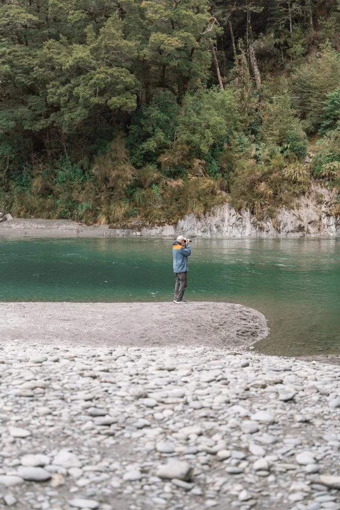 A person standing by the blue pools is holding up a camera taking a photo