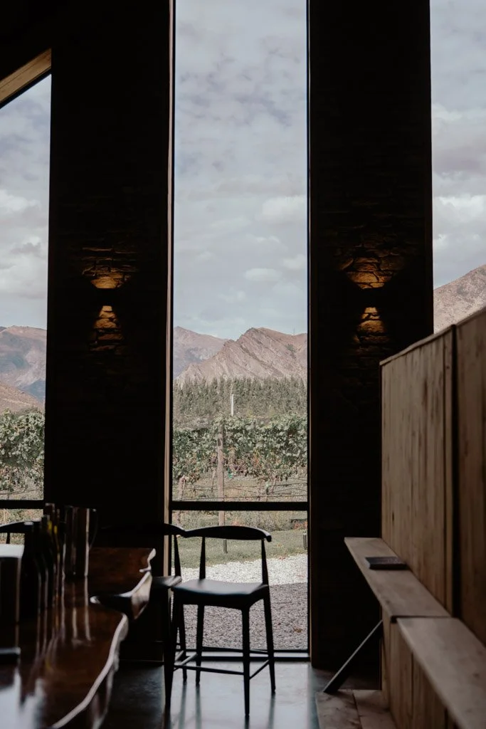 Floor to ceiling windows show views of rolling vines and mountains beyond them