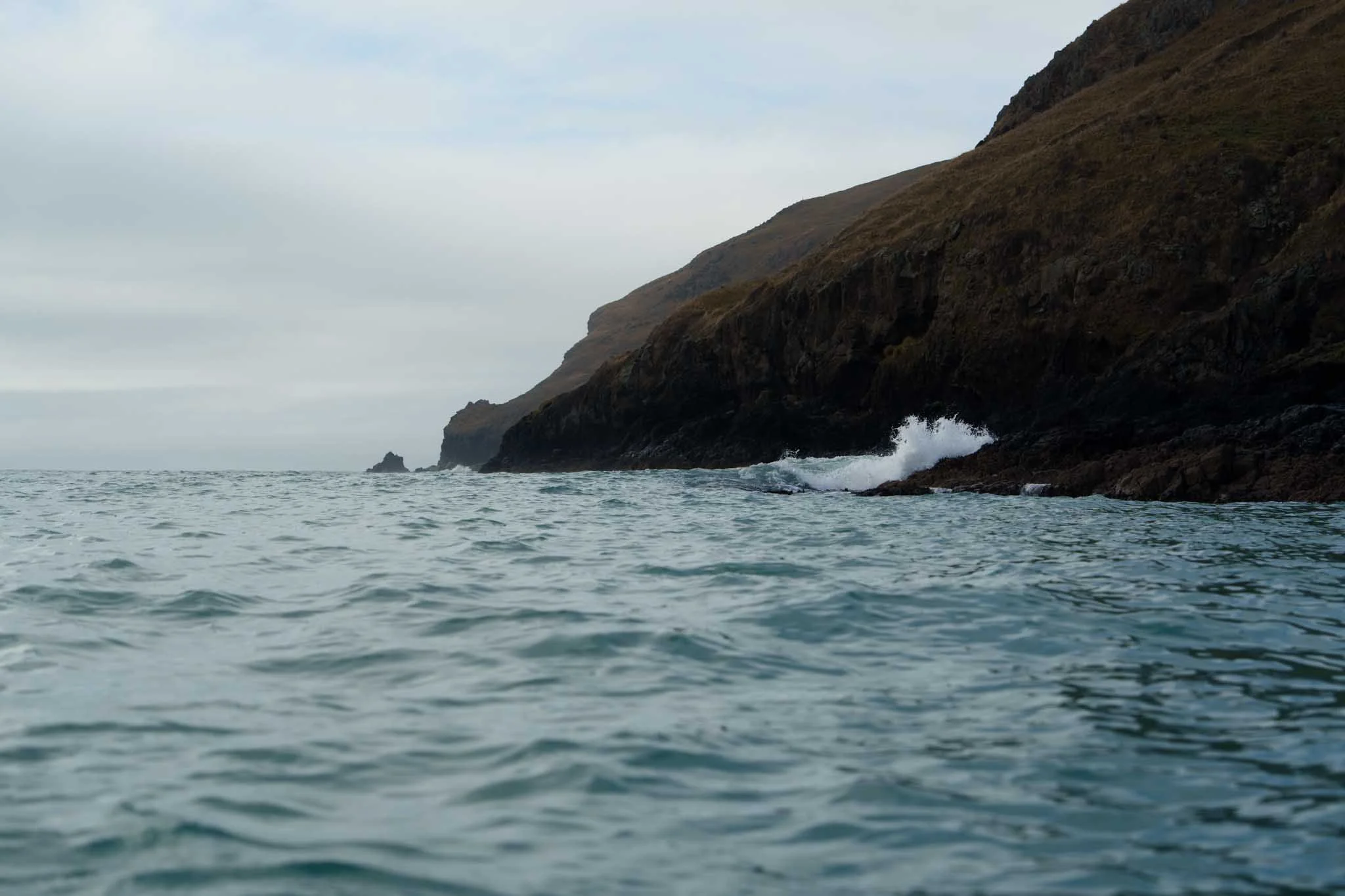Waves crash against sea cliffs above the turquoise waters of Banks Peninsula