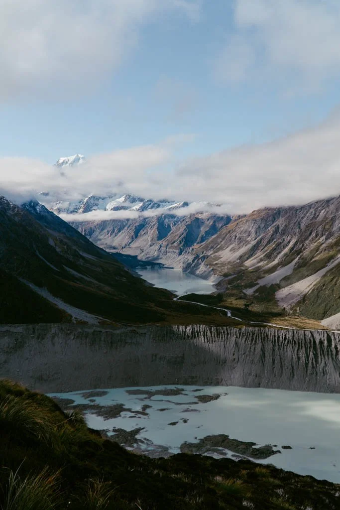 A moraine wall is above a pale green glacier lake, and beyond that a valley with a snow covered Aoraki/Mount Cook visible in the very distance
