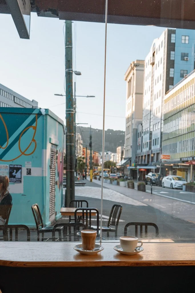 Coffee cups sit on a wooden bench in the window sill of a cafe in Wellington