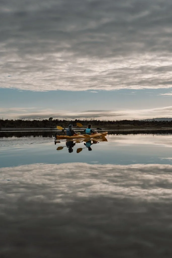 Kayakers paddle across the still surface of Okarito Lagoon