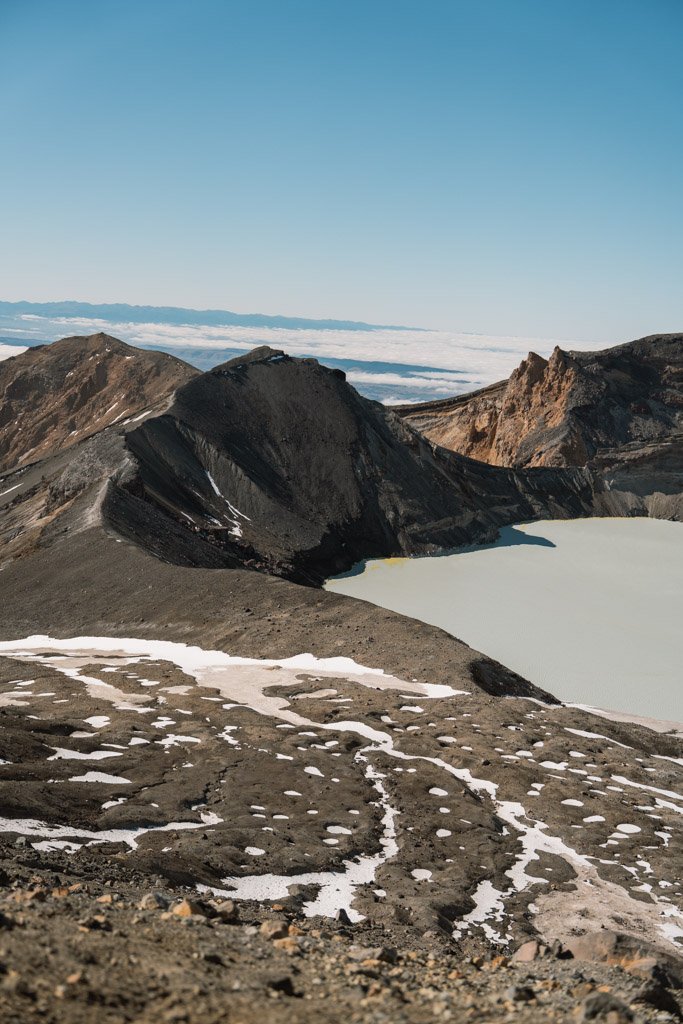 Patches of snow sit on rocks above a milky green volcanic crater lake