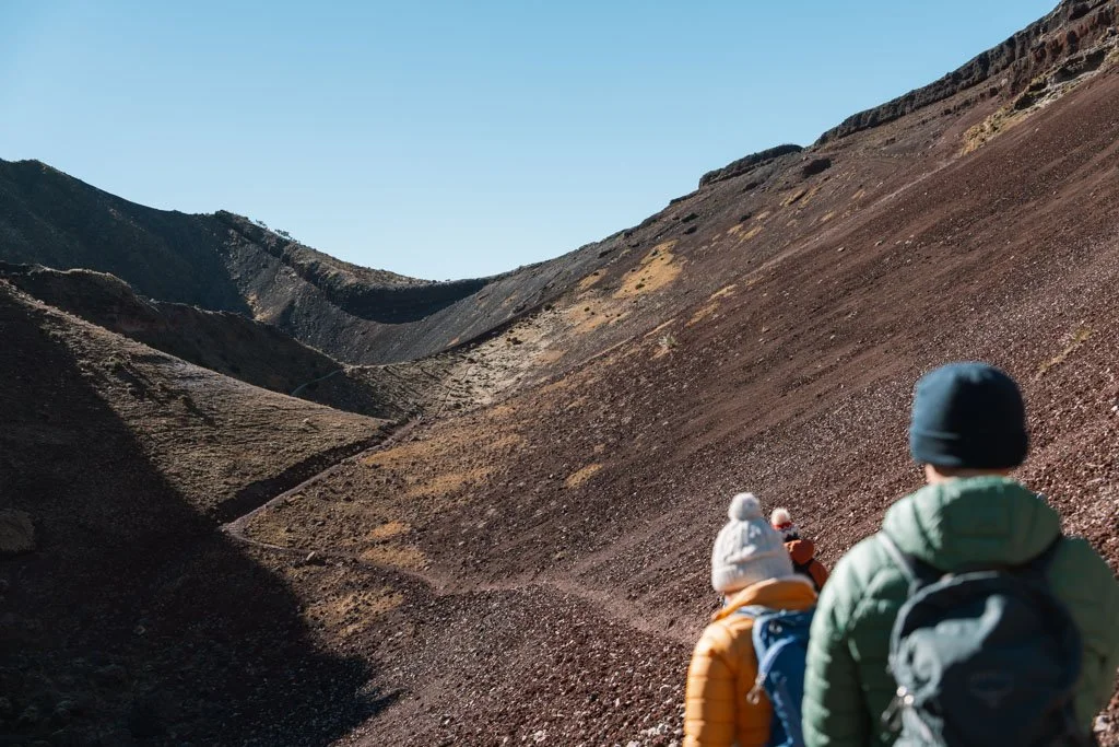 Hikers walk in single file up red scree at Mt Tarawera